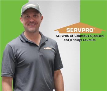 Man in SERVPRO shirt smiling at the camera on a green and white background 